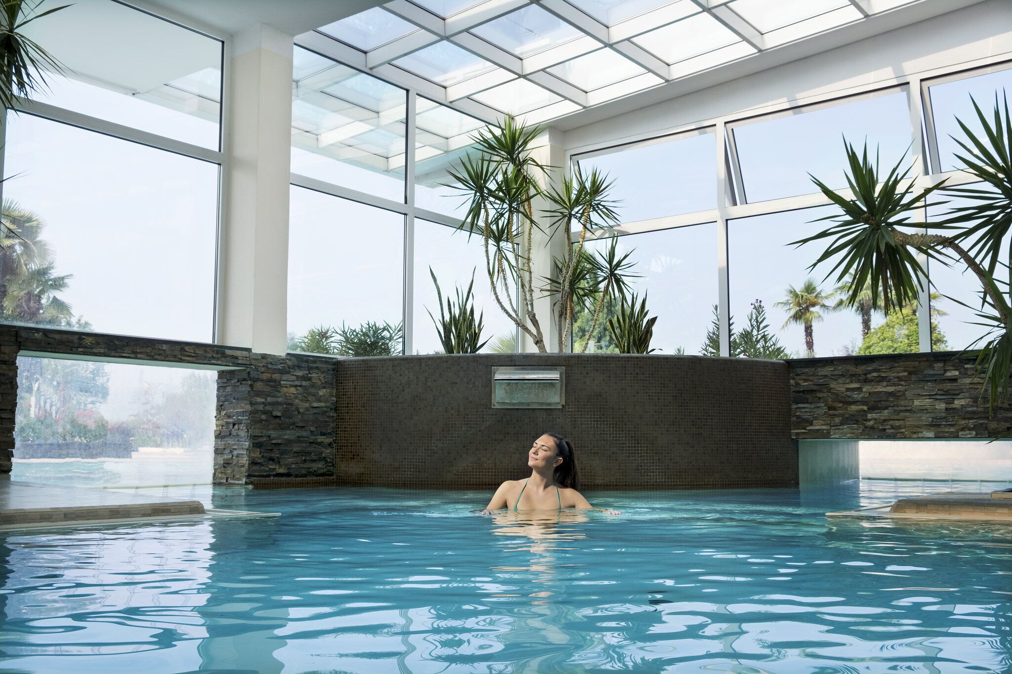 A person in a swimming pool with a glass ceiling and plants around.