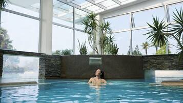 A person in a swimming pool with a glass ceiling and plants around.