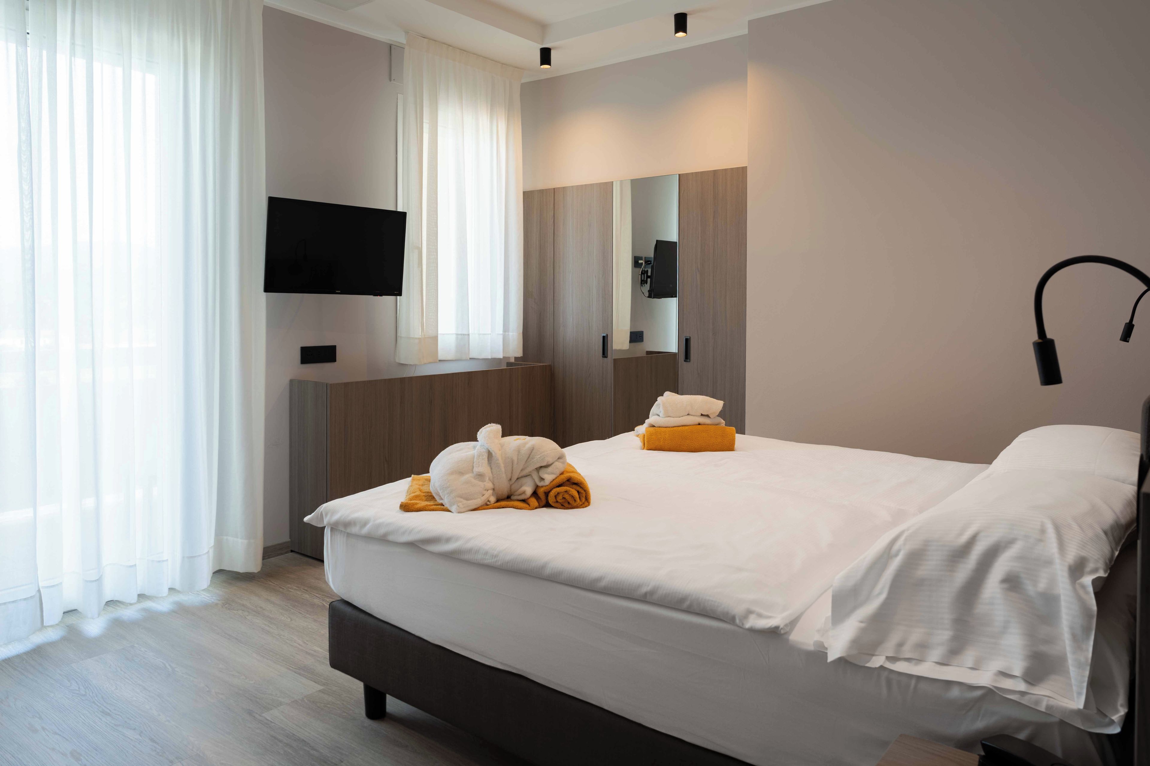 A hotel room with a bed, a flat-screen TV mounted on the wall, a bedside table, and a mirror.