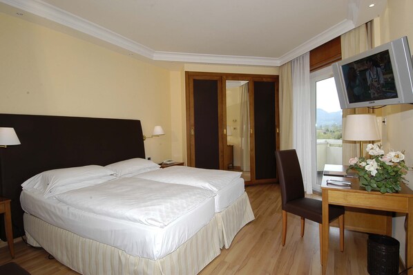 Habitación de hotel con cama doble, escritorio con silla, televisor y vista al exterior.