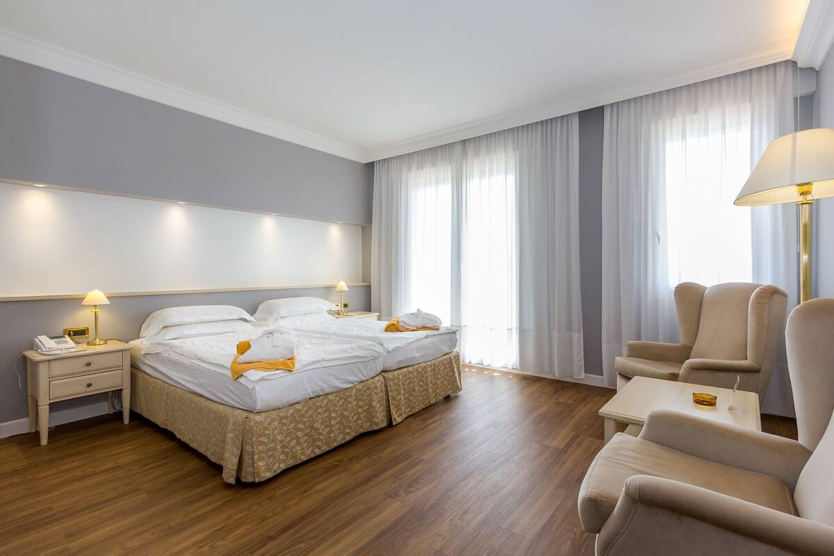 A hotel room with a bed, bedside tables, a lamp, a chair, and a small table.