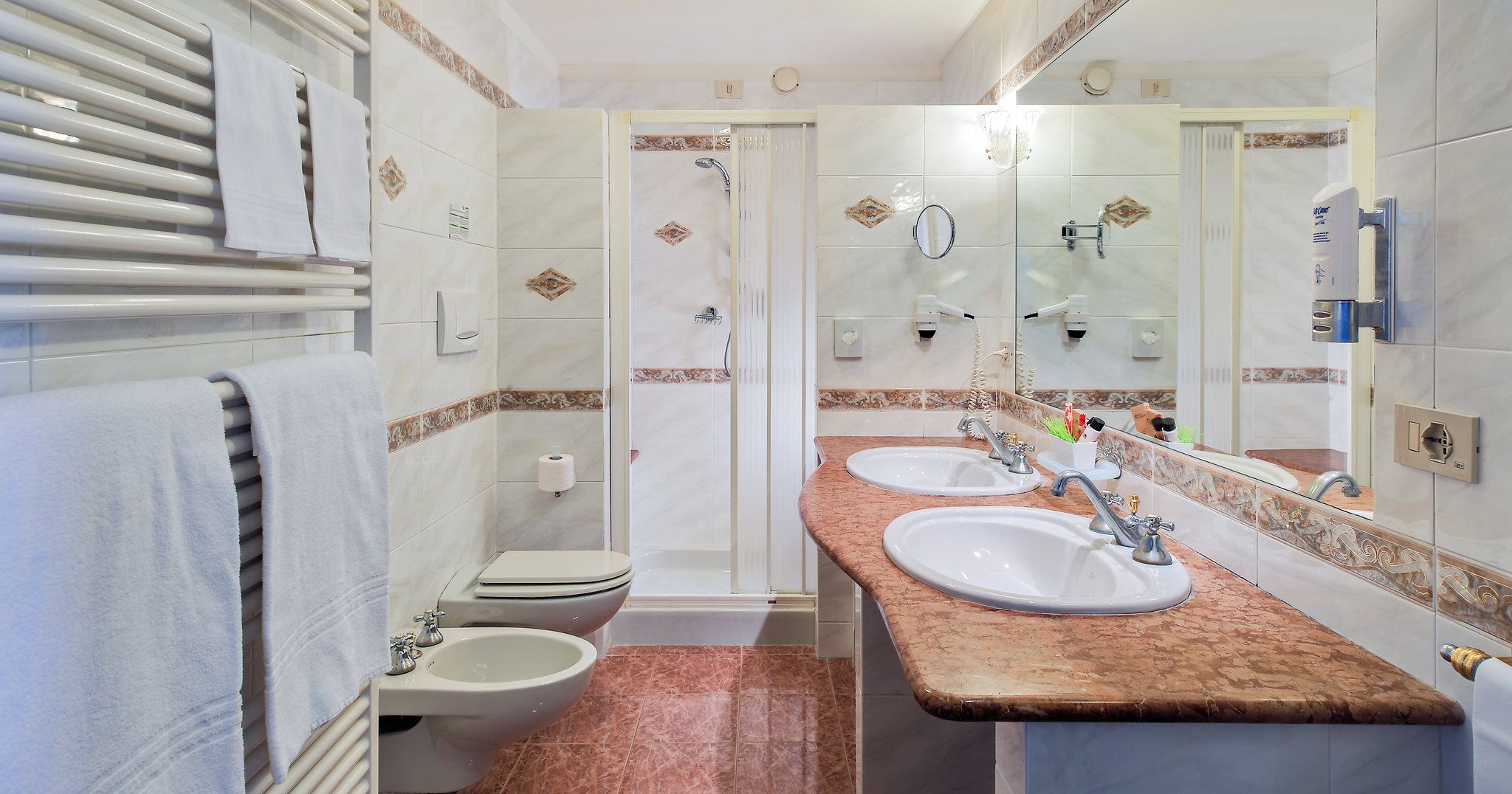 Een badkamer met twee wasbakken, toilet, bidet en douche.