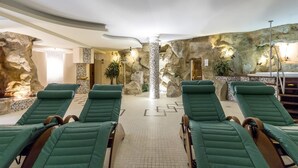 Un área de spa con sillones reclinables verdes, un pilar central y un muro de roca de fondo.