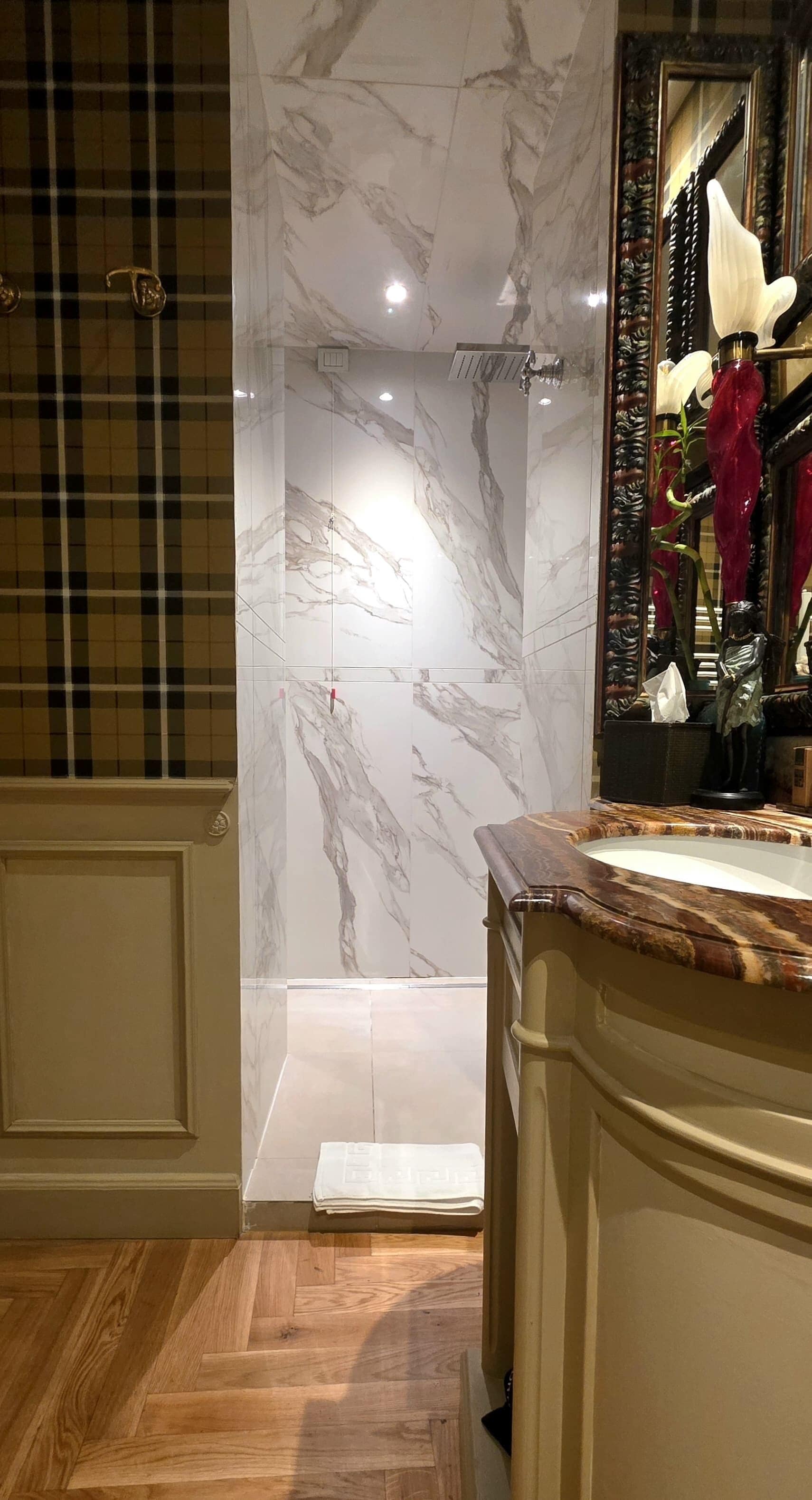 A bathroom with marble walls, a wooden floor, and a mirror with a decorative frame.