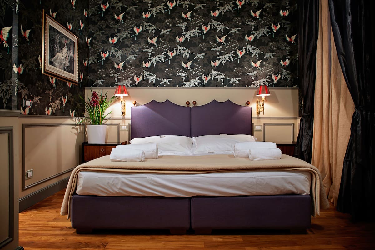 A neatly made bed with a purple headboard, a wall-mounted picture, and a decorative wall with a bird pattern.