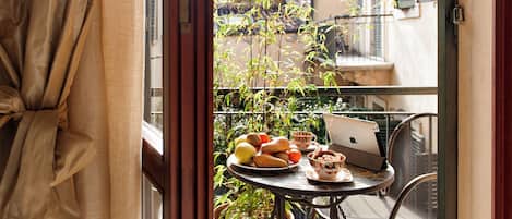 Un balcon avec une table préparée pour le petit-déjeuner, comprenant des fruits, des viennoiseries et un ordinateur portable.