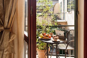 A balcony with a table set for breakfast, including fruits, pastries, and a laptop.