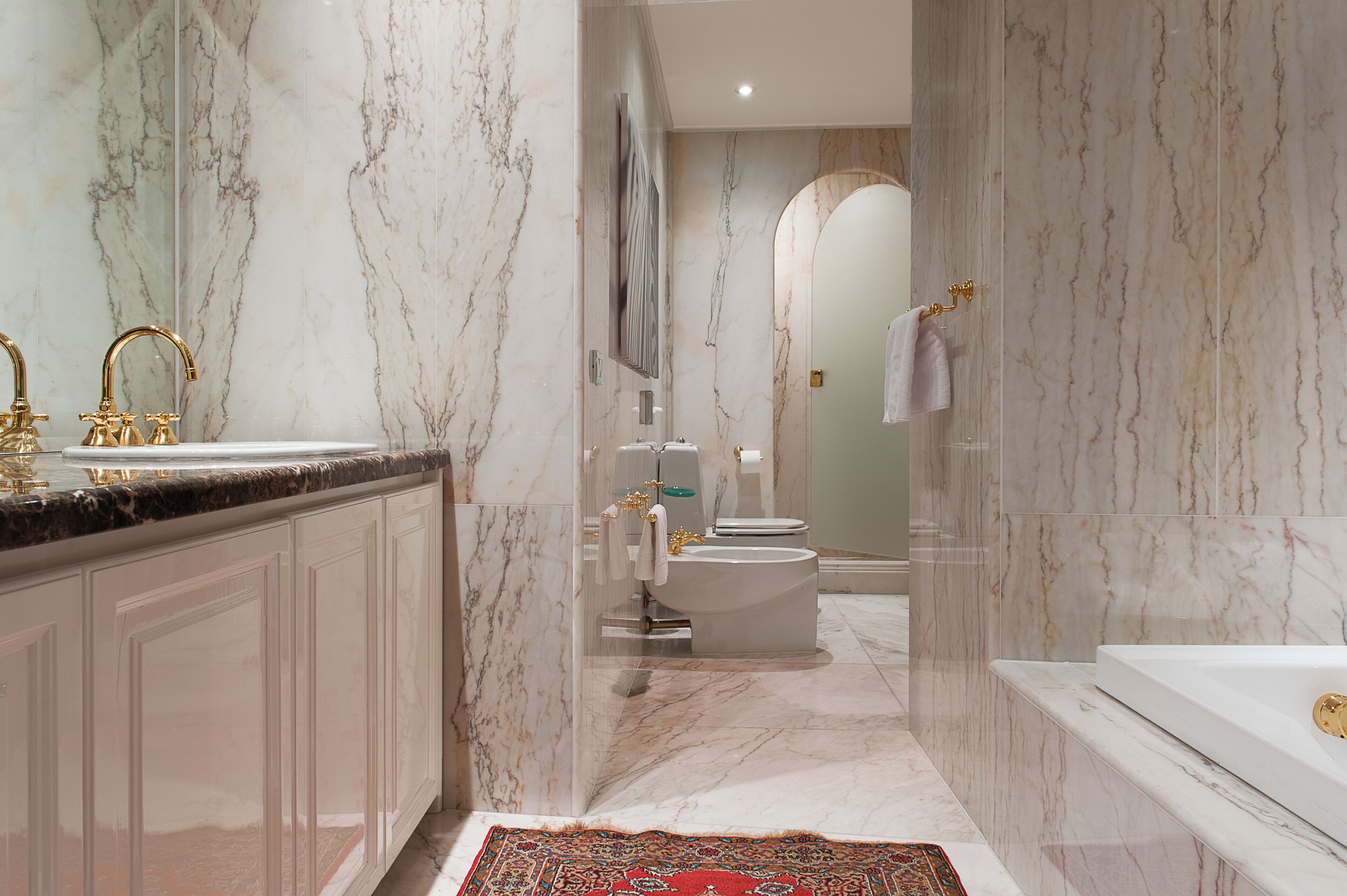 Ein modernes Badezimmer mit Marmorwänden, einer Badewanne, einer Toilette und einem Waschbecken mit goldenen Armaturen.
