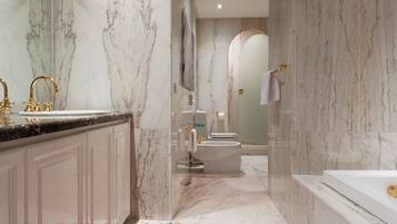 Ein modernes Badezimmer mit Marmorwänden, einer Badewanne, einer Toilette und einem Waschbecken mit goldenen Armaturen.