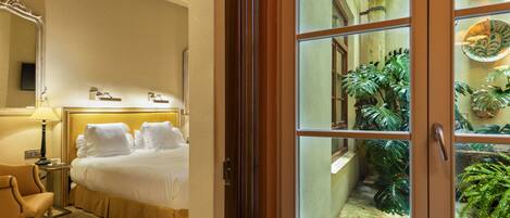 A hotel room with a bed, a chair, a lamp, and a window with a view of a garden.