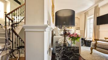 A staircase with a bicycle, a marble pedestal table with a lamp, and a sofa in a well-lit room.