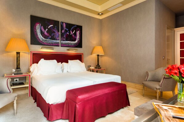 A hotel room with a large bed, two bedside tables with lamps, a chair, and a desk with a vase of flowers.