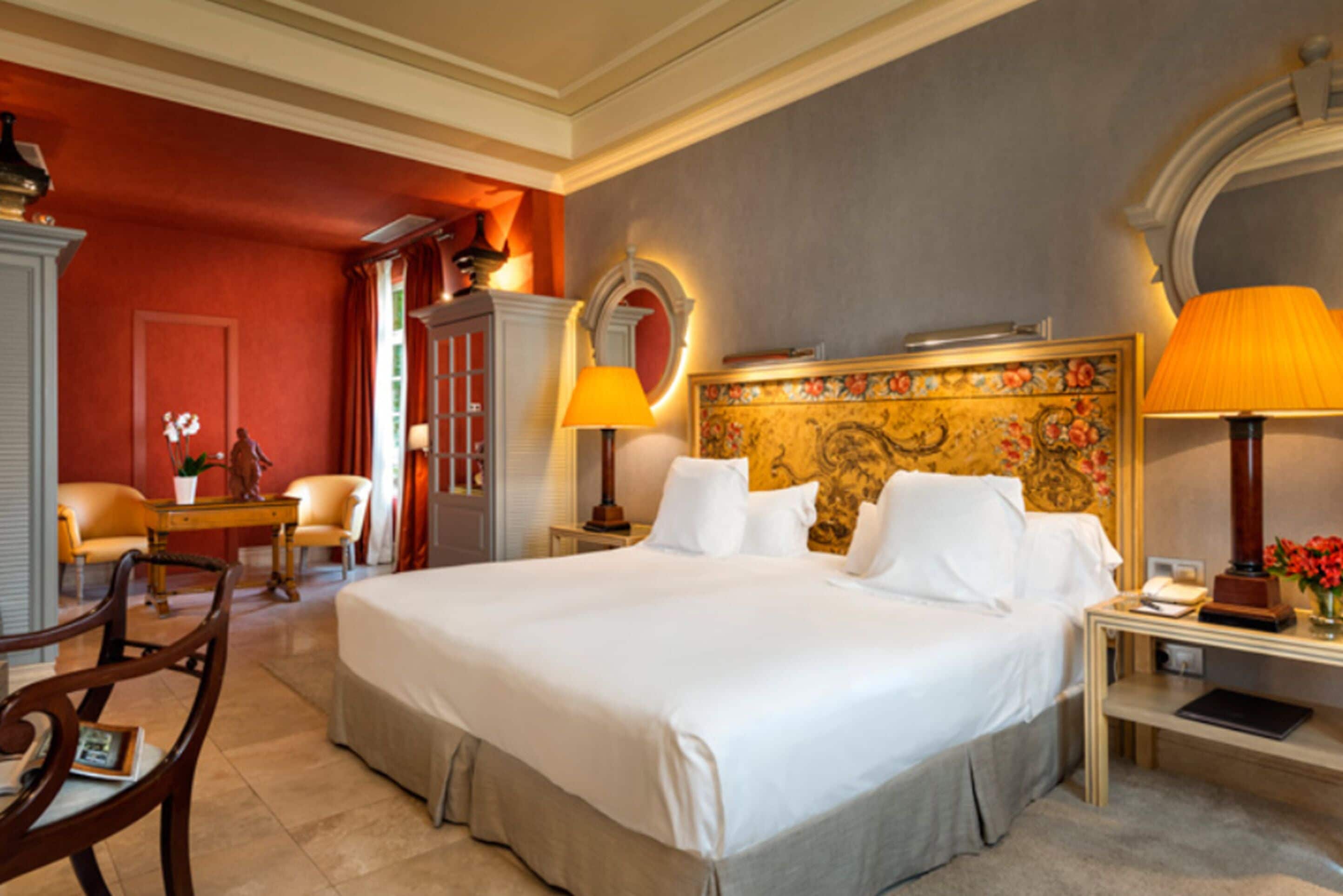 A spacious hotel room with a large bed, two bedside lamps, a wooden nightstand, a chair, and a desk with a lamp.
