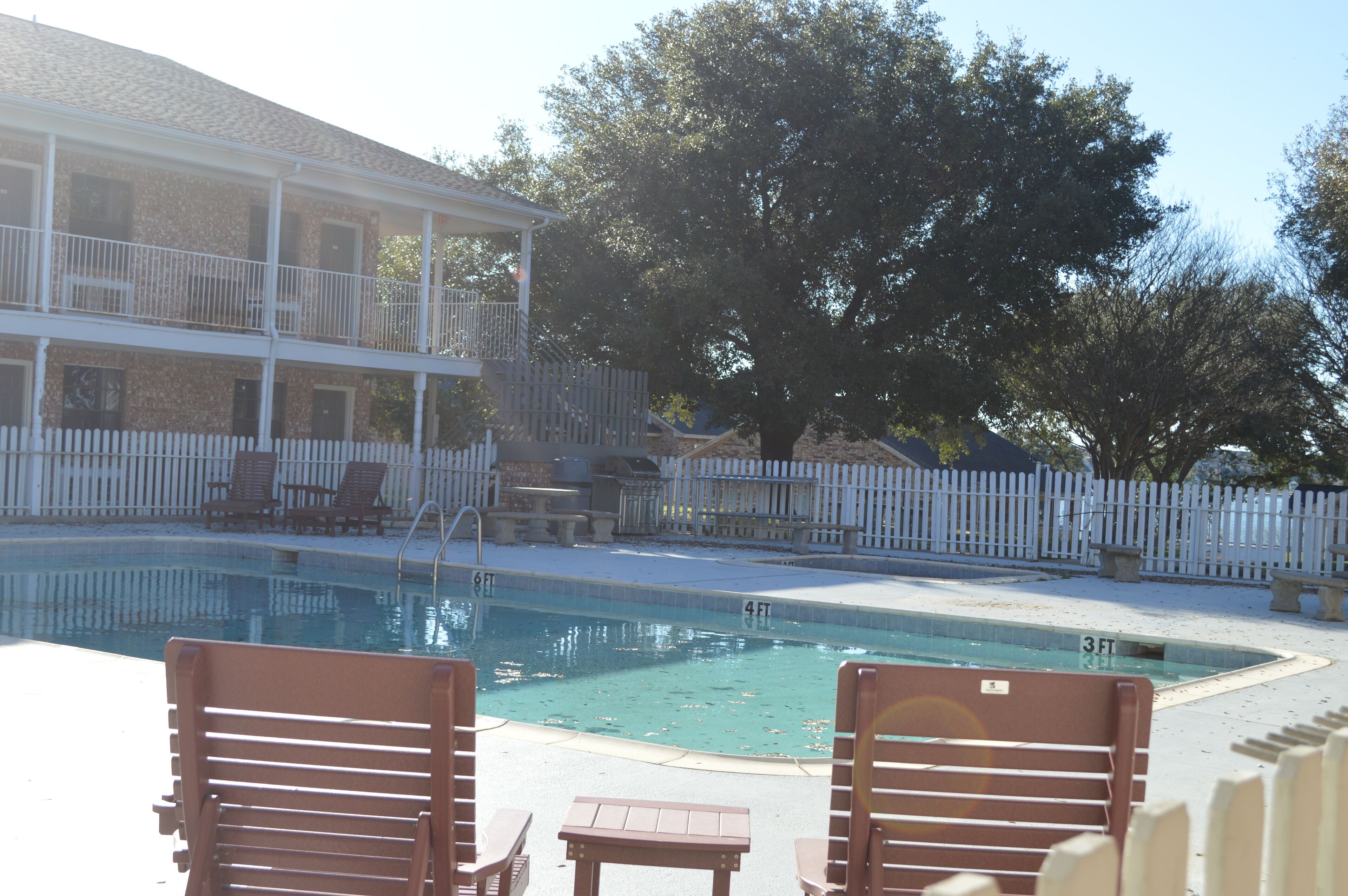 A pool area with lounge chairs and a building with a balcony.