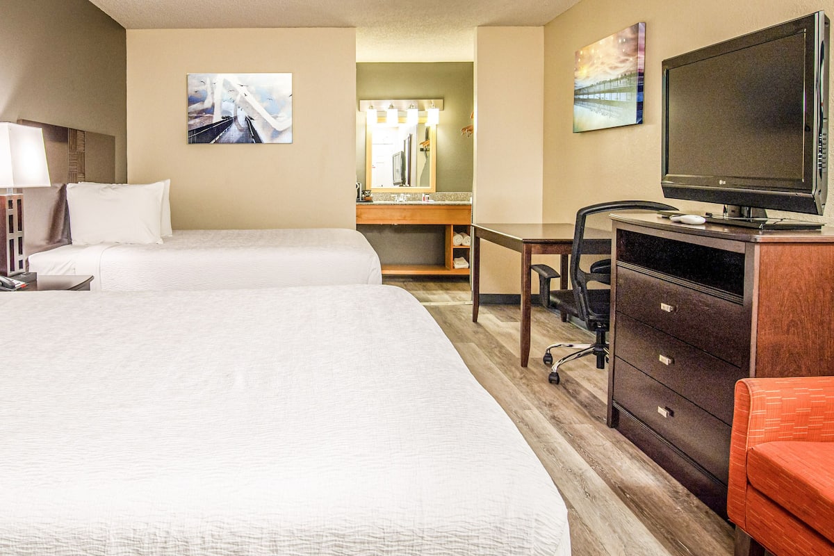 A hotel room with two beds, a desk, a television, and a bathroom visible in the background.