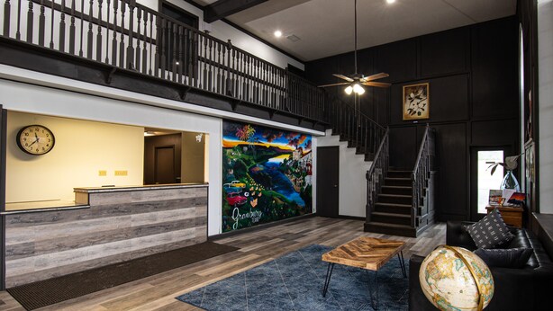 A modern reception area with a wooden reception desk, a large mural, and a staircase leading to an upper level. - Lake View Inn (Granbury)