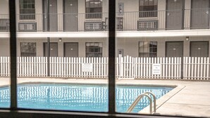 A pool area with a white fence, a lifeguard sign, and a building with multiple doors and windows in the background.