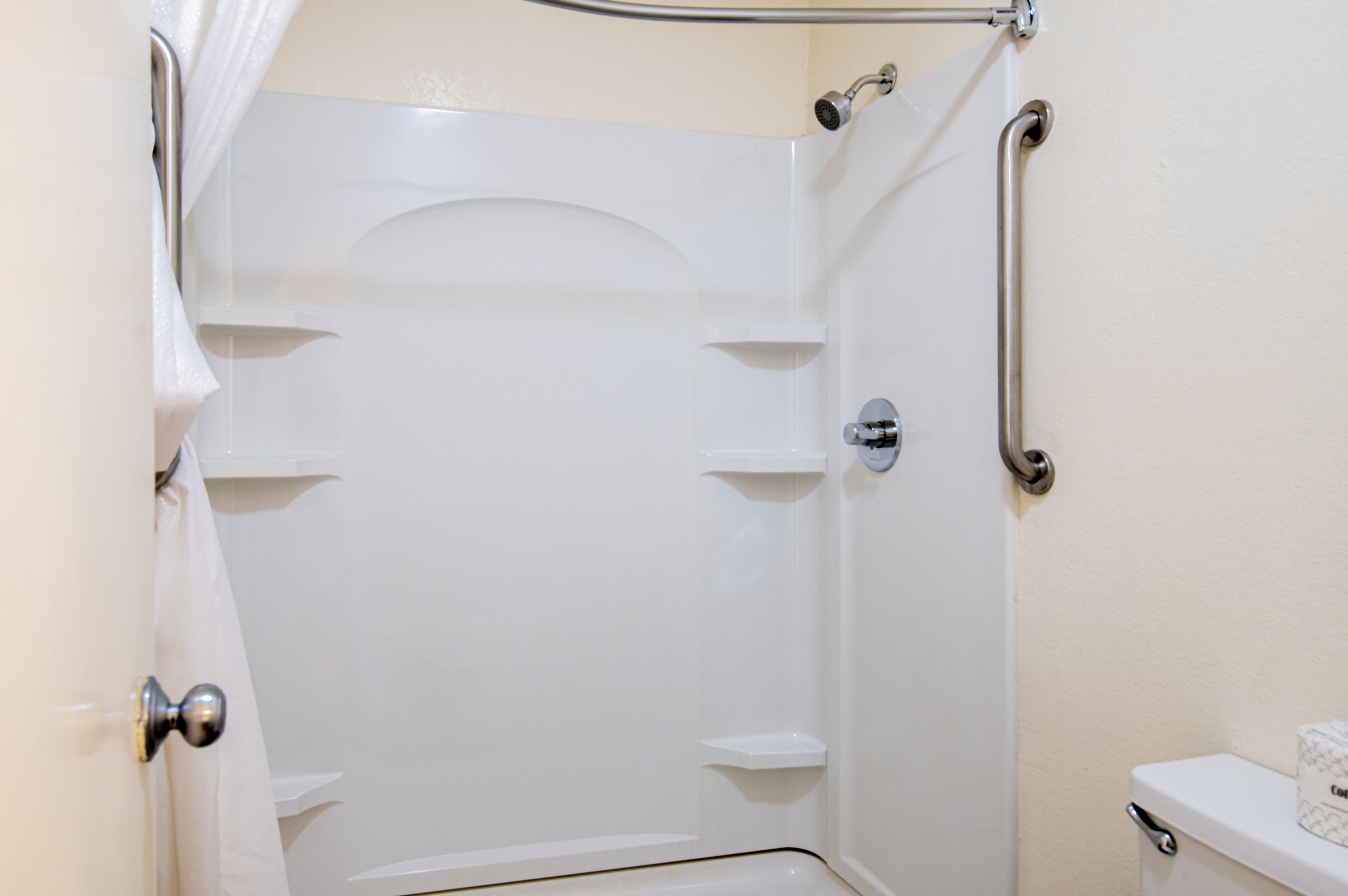 Un box de ducha blanco con puerta, barandilla y toallero.