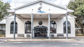 A building with a white facade, large arched windows, and a central entrance with a decorative emblem. - Lake View Inn (Granbury)