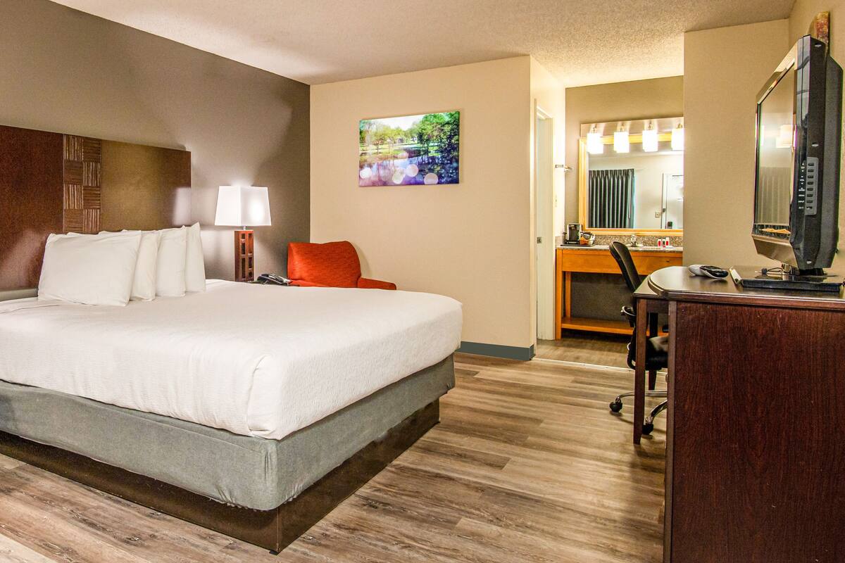 A hotel room with a large bed, two bedside tables, a desk with a chair, a mirror, and a television.