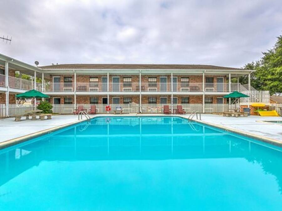 Una piscina con un edificio de ladrillo al fondo, un área cercada y un parque infantil.