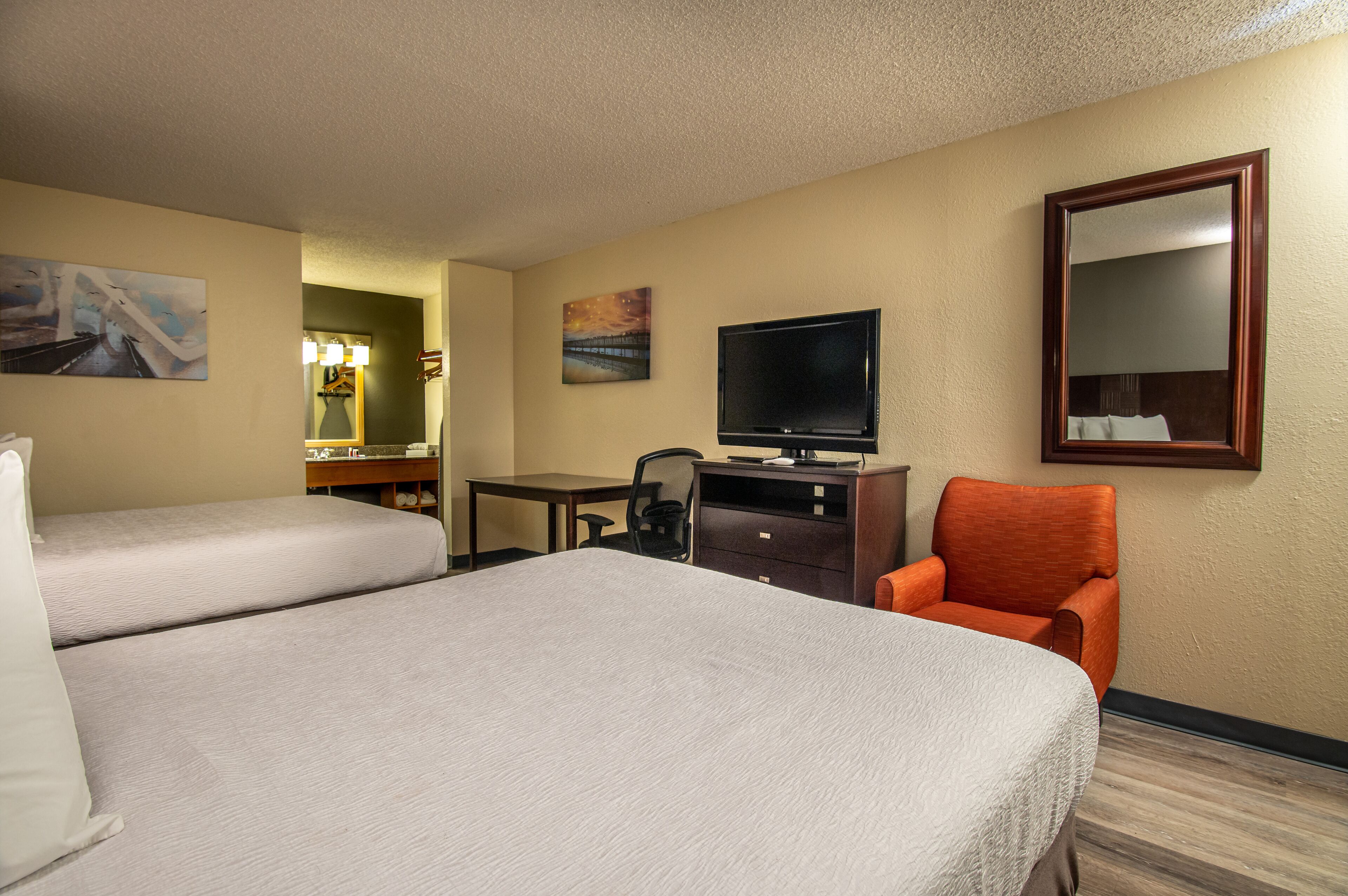A hotel room with two beds, a desk, a television, a chair, and a mirror.