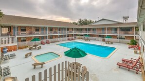 A hotel with a pool area, including a hot tub, lounge chairs, and umbrellas.