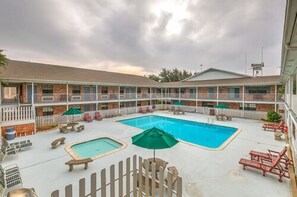 A hotel with a pool area, including a hot tub, lounge chairs, and umbrellas.