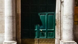Une grande porte richement décorée, de couleur verte, surmontée d’un emblème représentant une couronne et flanquée de deux colonnes.