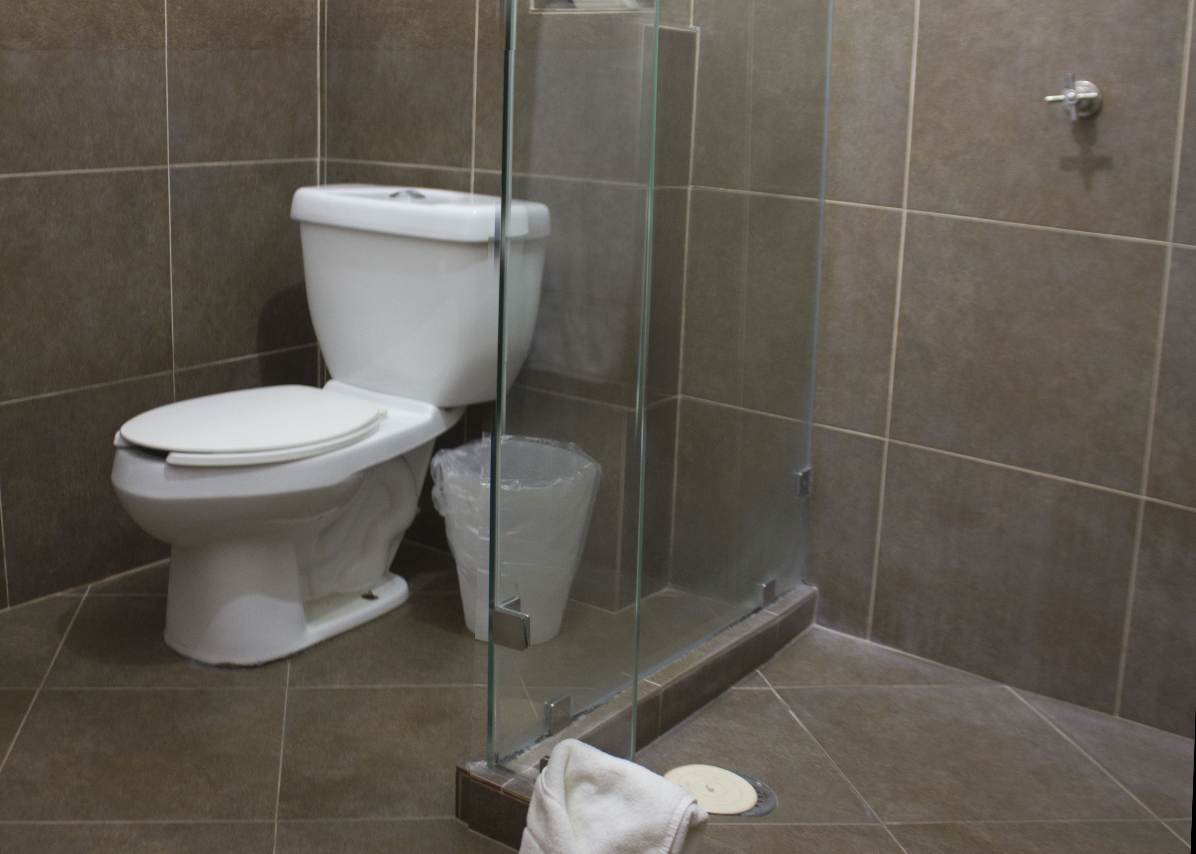 Un baño con inodoro, cabina de ducha de vidrio y un cubo de basura.