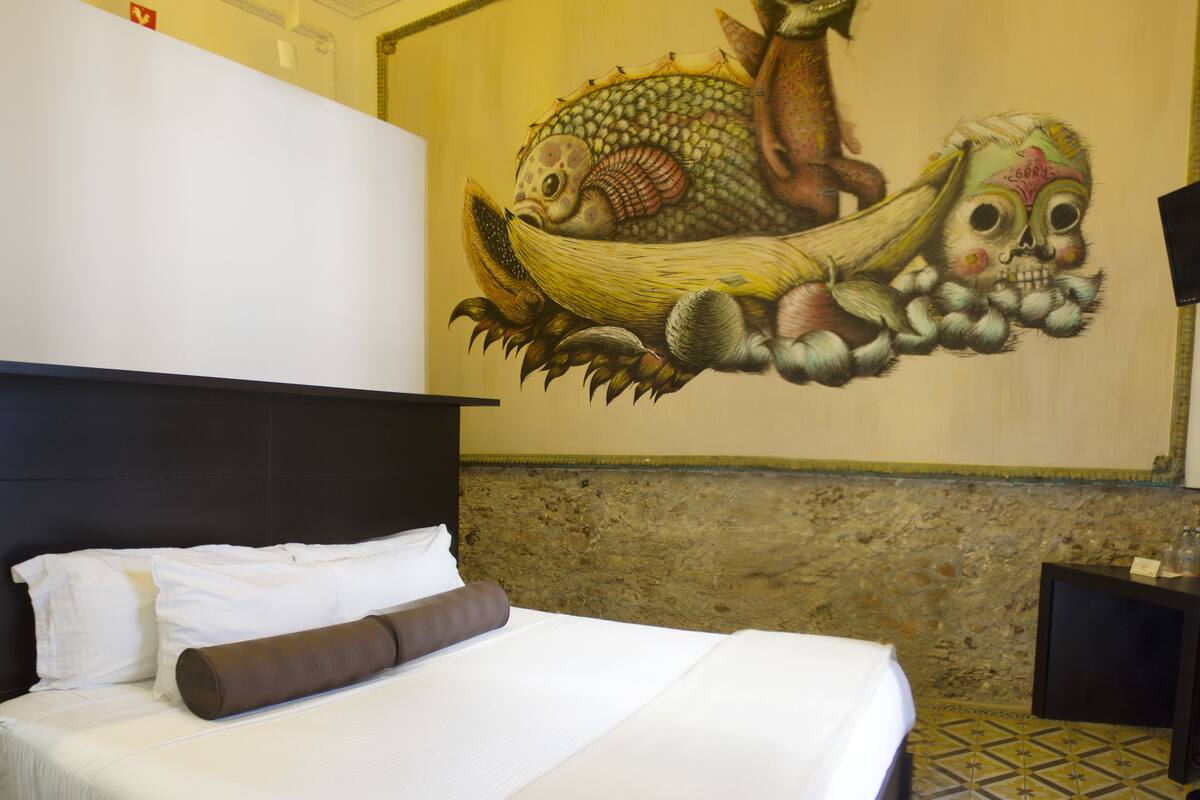 Una habitación de hotel con una cama, un mural en la pared y un muro de piedra.