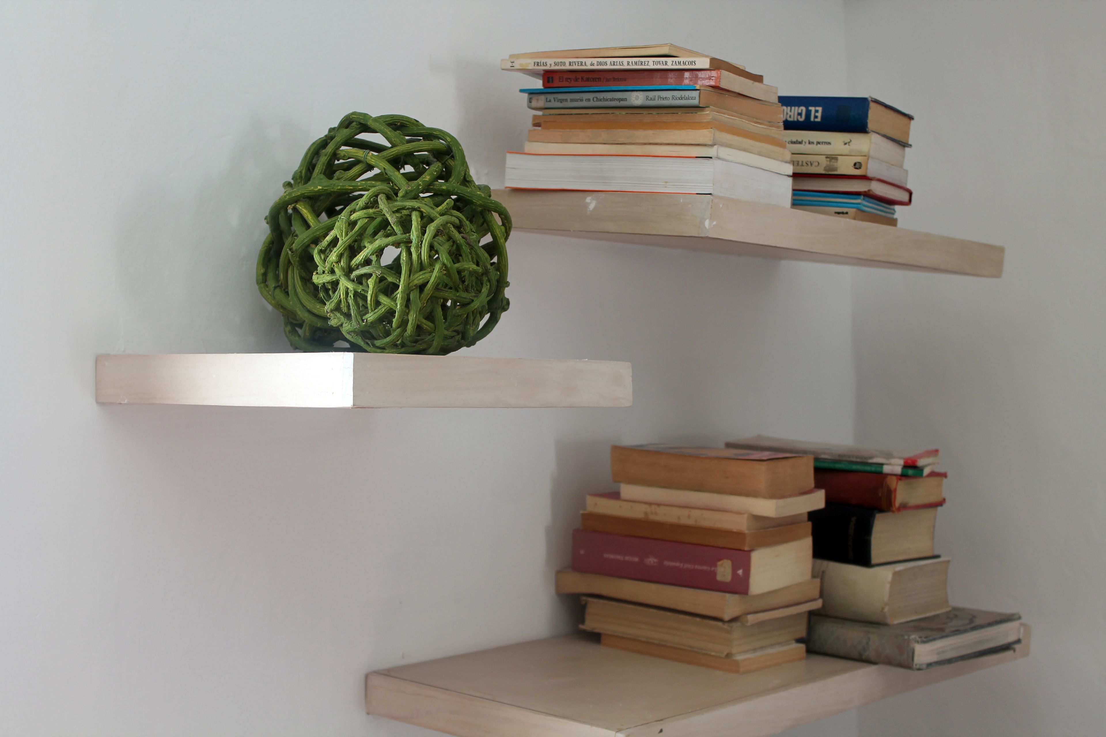 A wall with three wooden shelves, each holding books and a green spherical object.