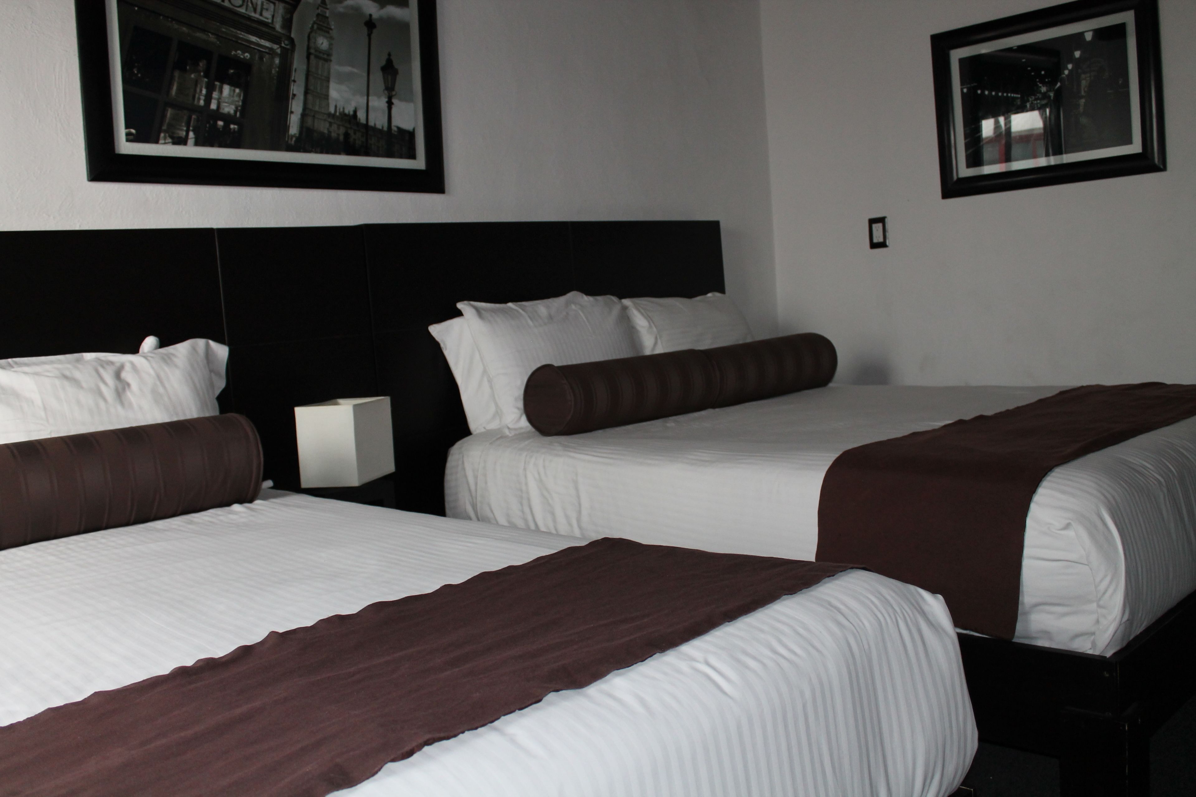 A hotel room with two beds, a nightstand, and framed pictures on the wall.