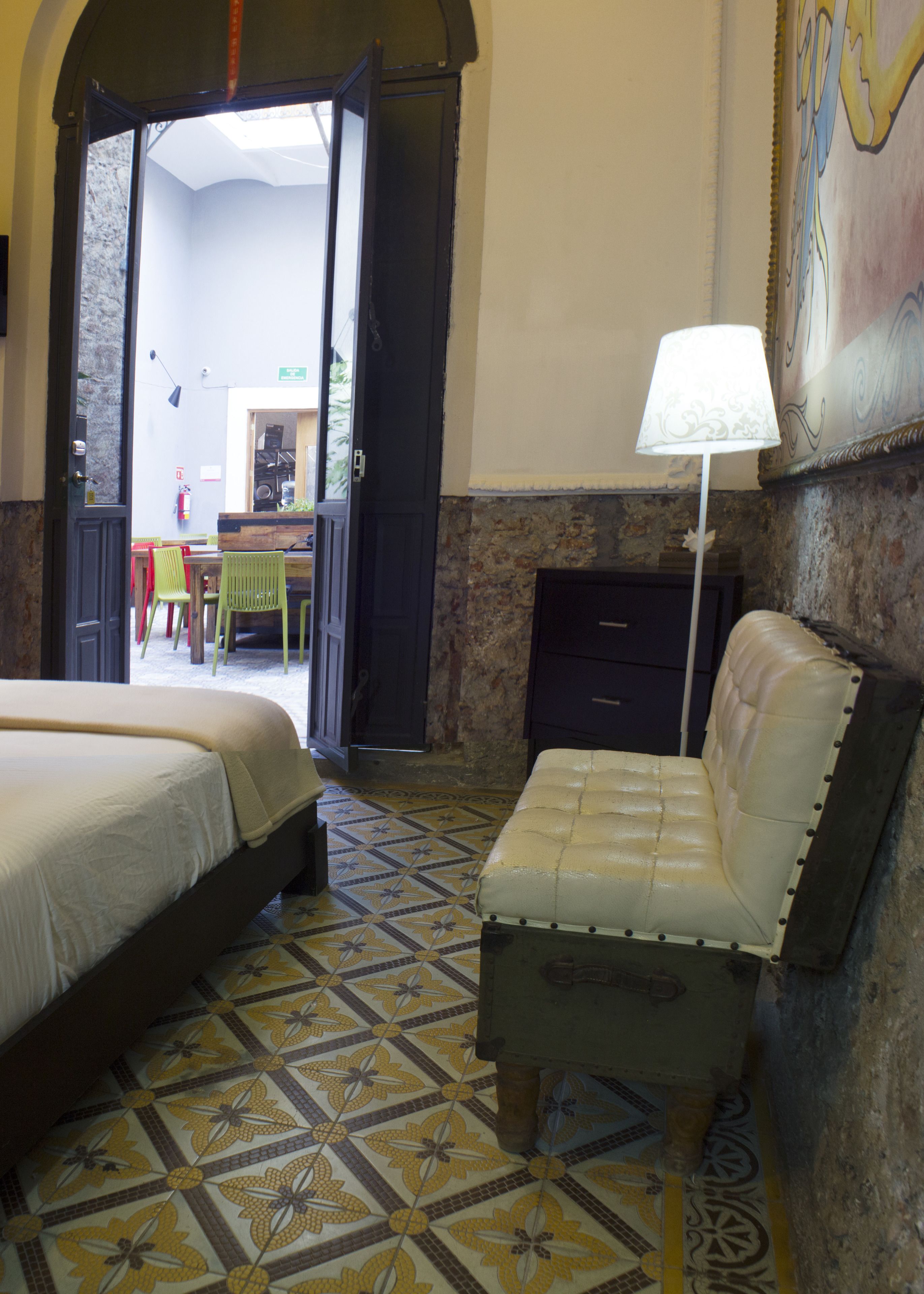A hotel room with a bed, a chair, a lamp, and a tiled floor.