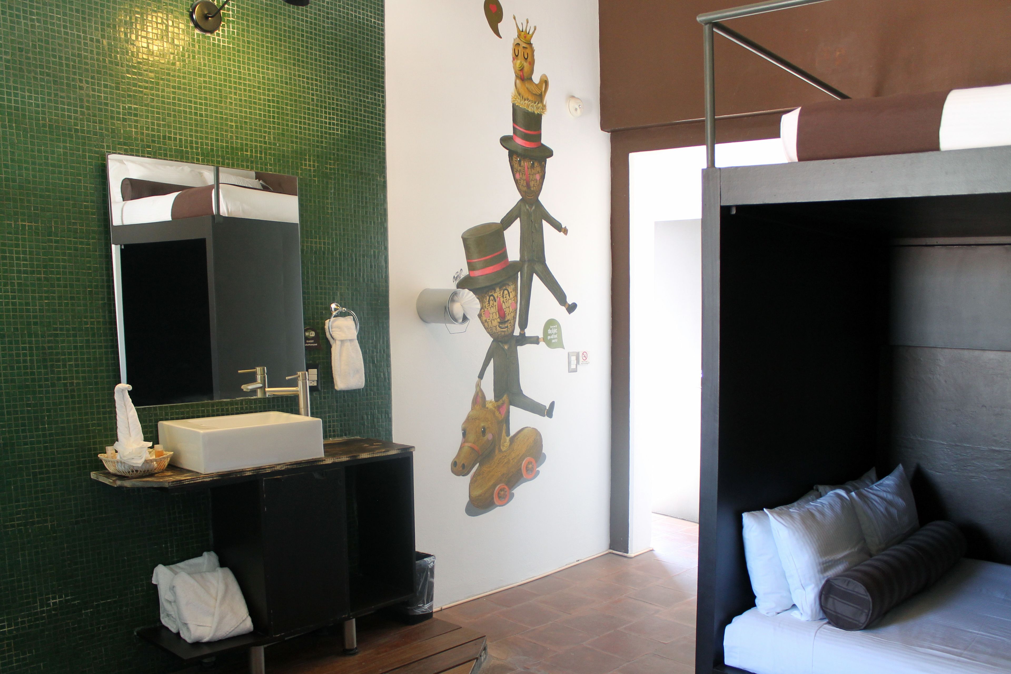 A bathroom with a green tiled wall, a sink, a mirror, and a wall decal of a cartoon character.