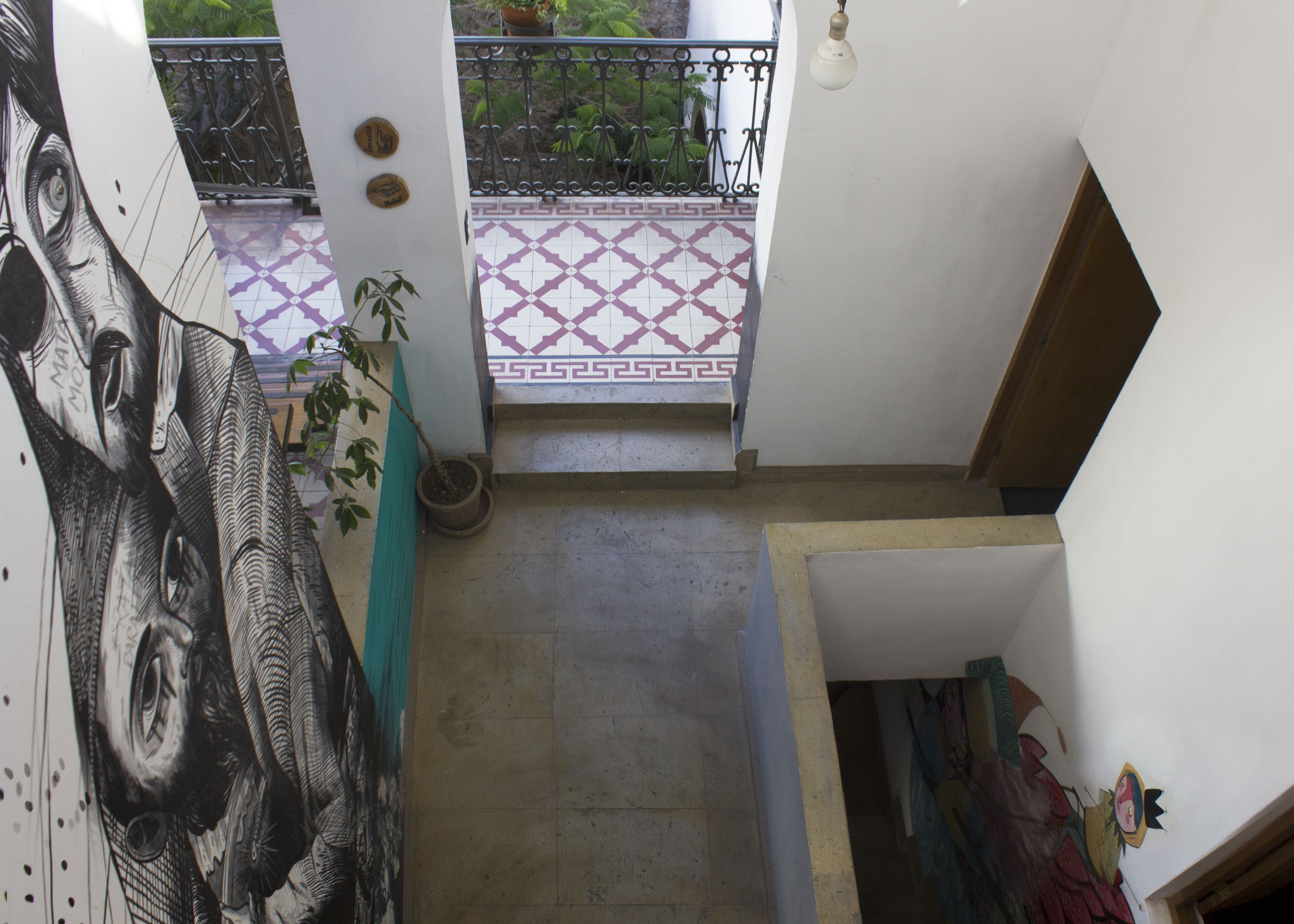 A staircase leading to a balcony with patterned tiles, a potted plant, and a wall with a large mural.