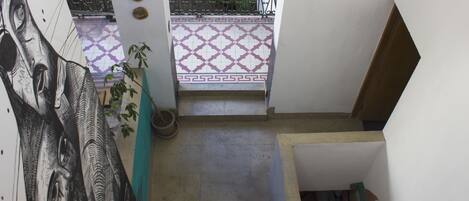 A staircase leading to a balcony with patterned tiles, a potted plant, and a wall with a large mural.