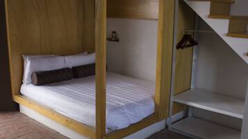 A single bed with a wooden frame and white bedding, a small shelf with a cup and a hanger, and a staircase with wooden steps.