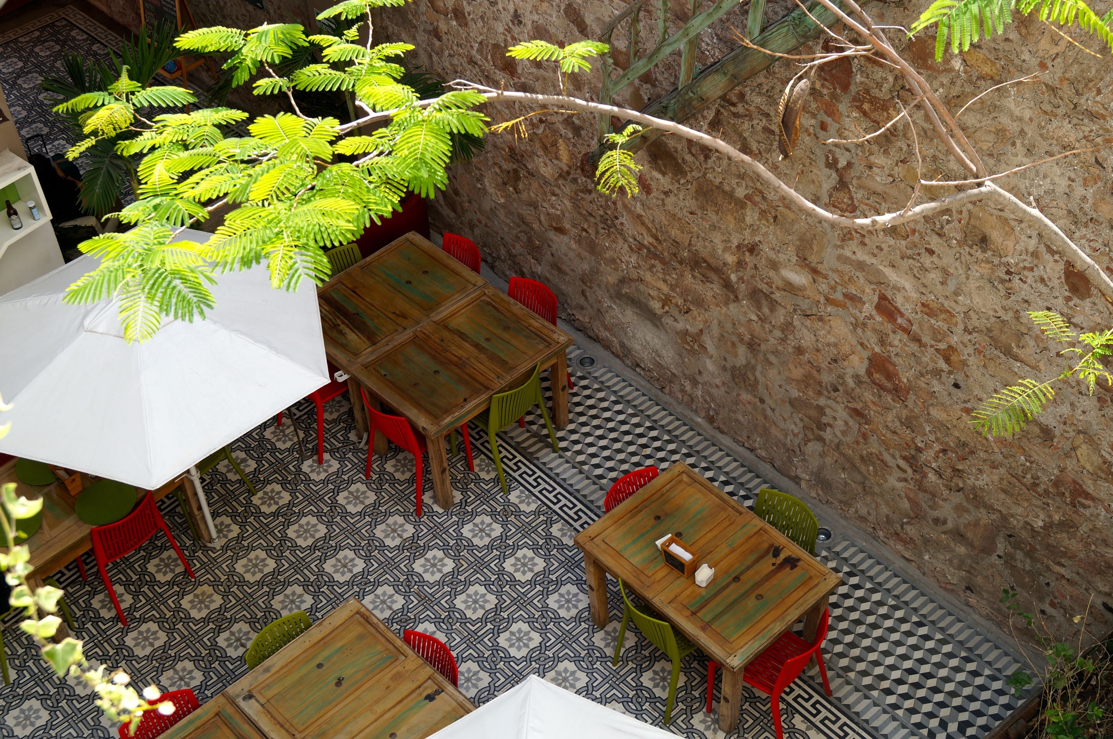 An outdoor patio with wooden tables and chairs, a patterned floor, and a stone wall.