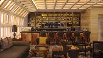 Zona de bar con diversas opciones de asientos, incluyendo sofás y sillones, y una barra bien surtida con numerosas botellas.