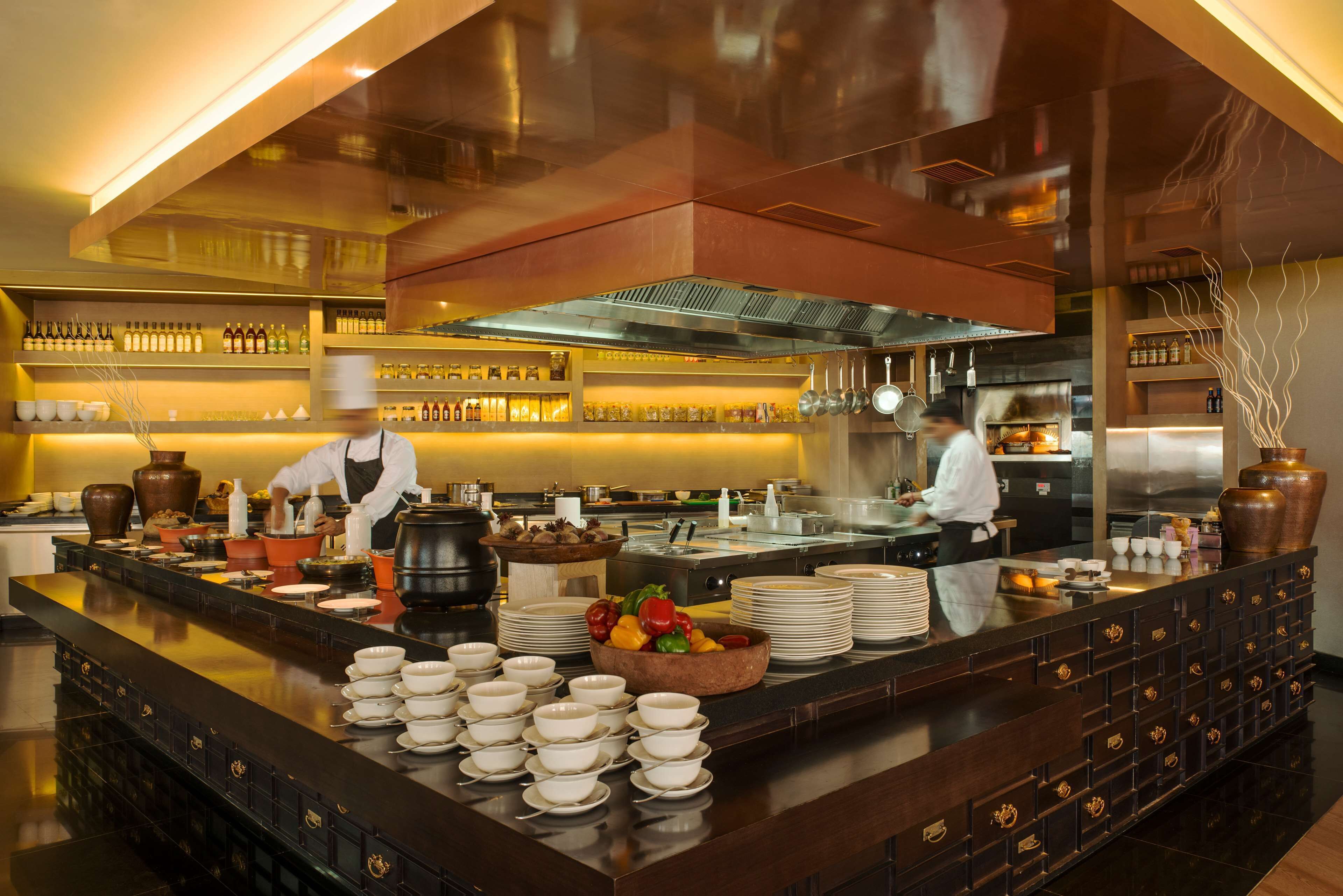 A modern kitchen with chefs preparing food, equipped with stainless steel appliances and a variety of cooking utensils.