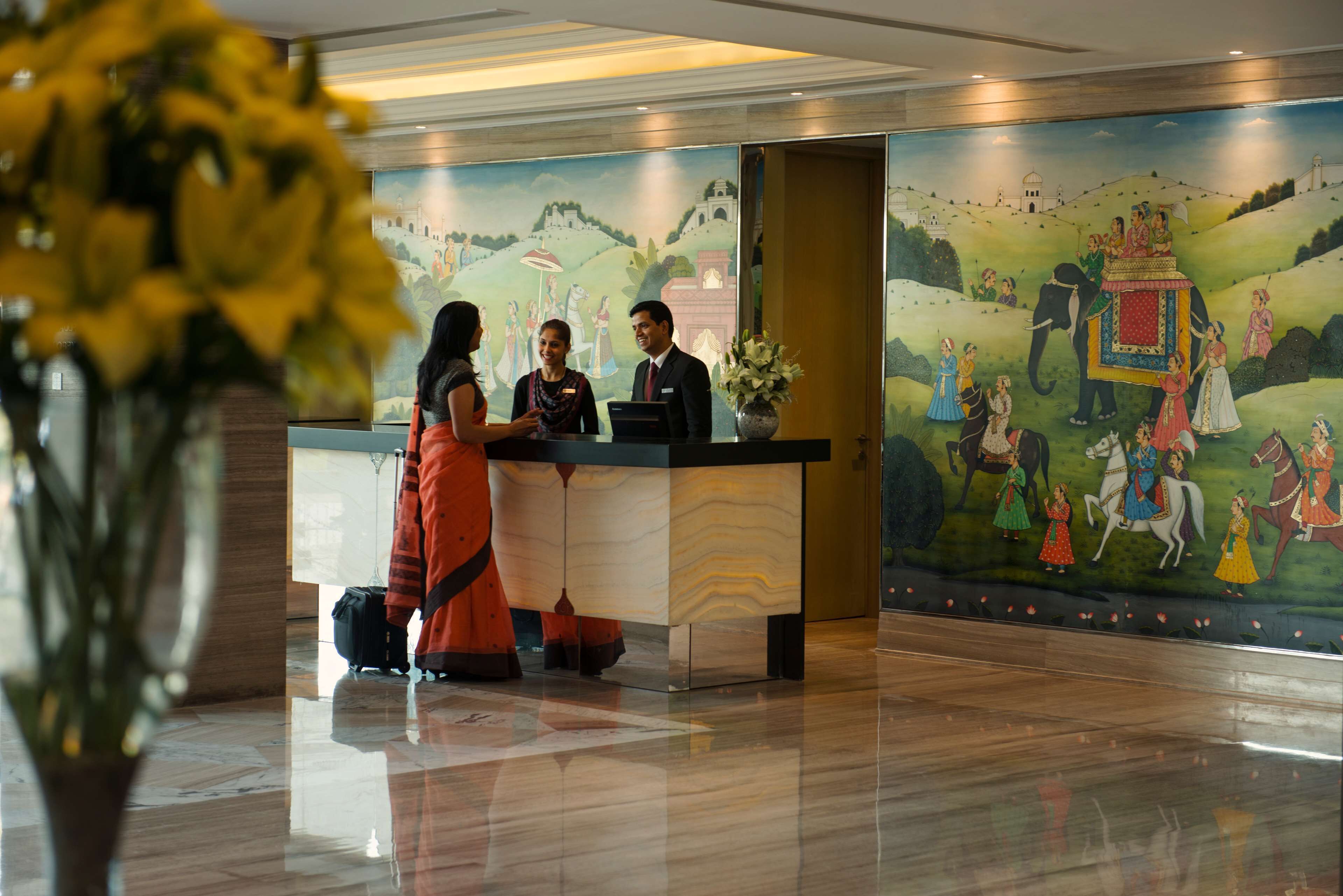 A reception desk with a mural depicting traditional scenes, a vase with flowers, and a polished floor.