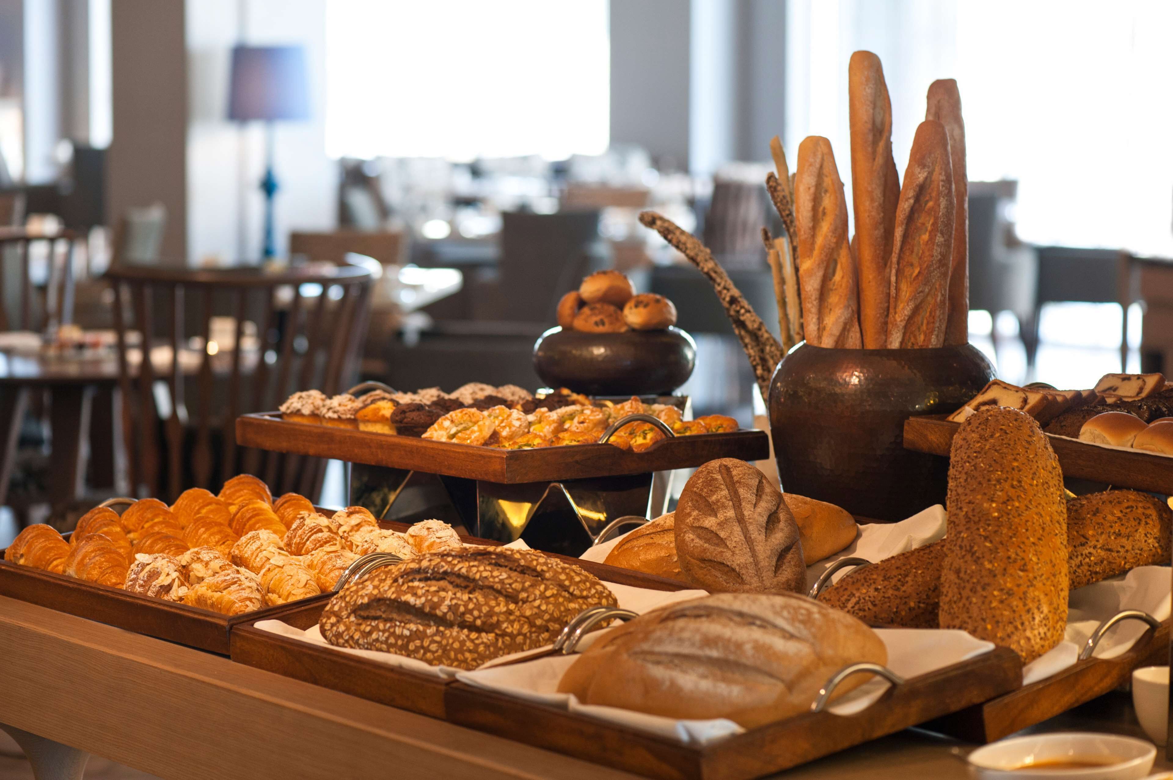 A variety of breads and pastries displayed on wooden trays in a well-lit room with tables and chairs in the background.