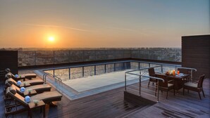 A rooftop terrace with sun loungers, a pool, and a dining area with a view of the sunset. - Hyatt Regency Ludhiana (Ludhiana)