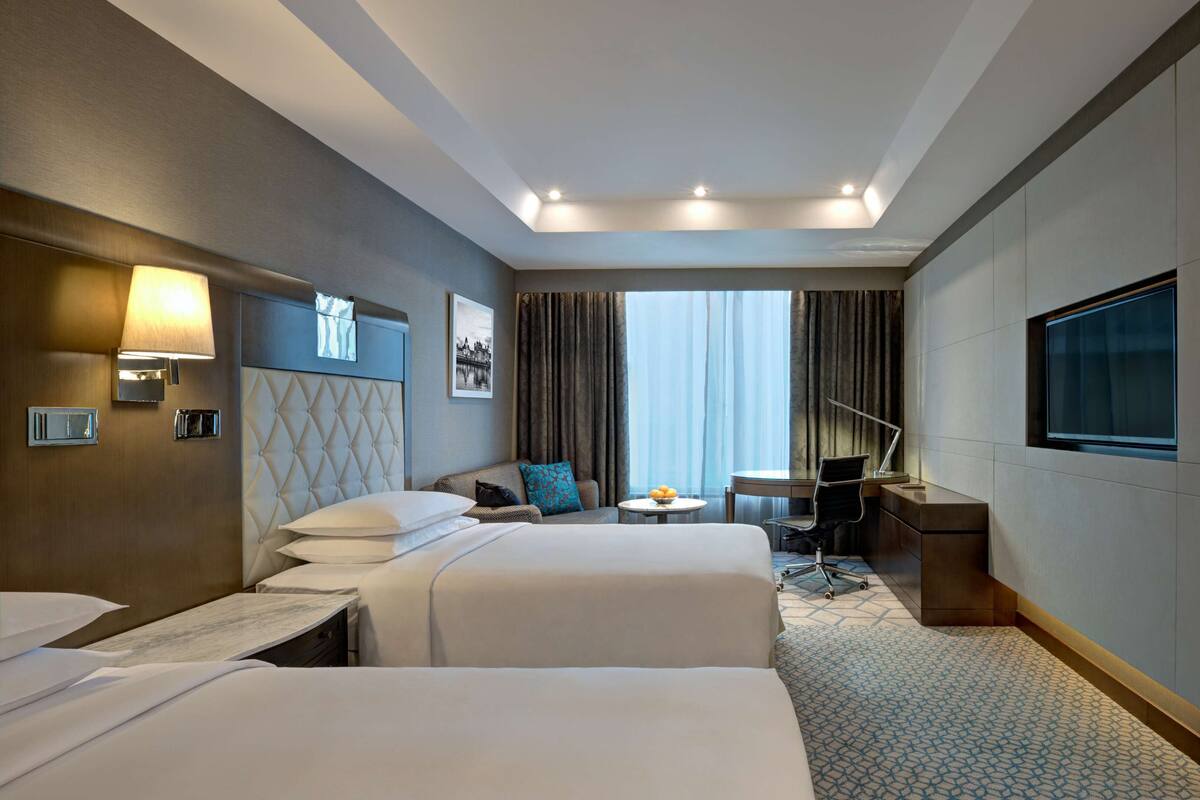 Habitación de hotel con dos camas, un escritorio, una silla, un televisor y una ventana con cortinas.