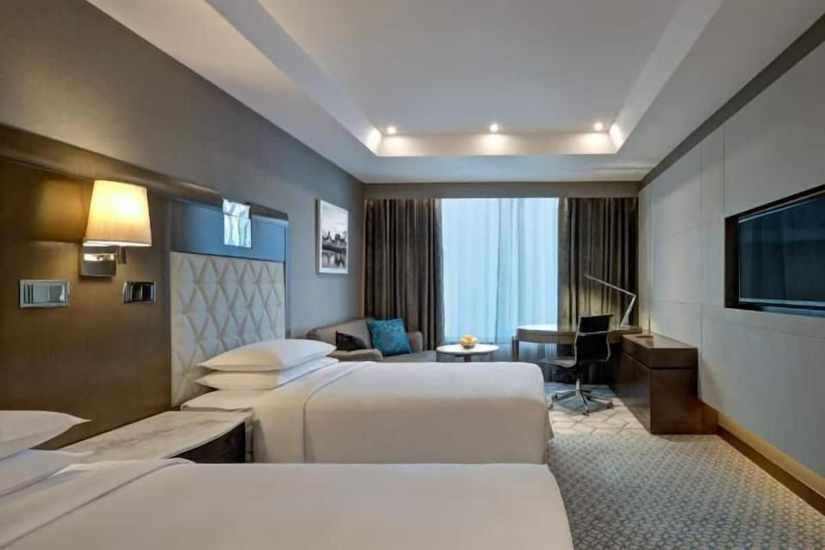 Habitación de hotel con dos camas, un escritorio, una silla, un televisor y una ventana con cortinas.