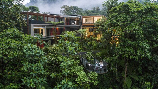 A modern house with a glass bridge connecting two levels, surrounded by dense greenery. - Mashpi Lodge (Pacto)