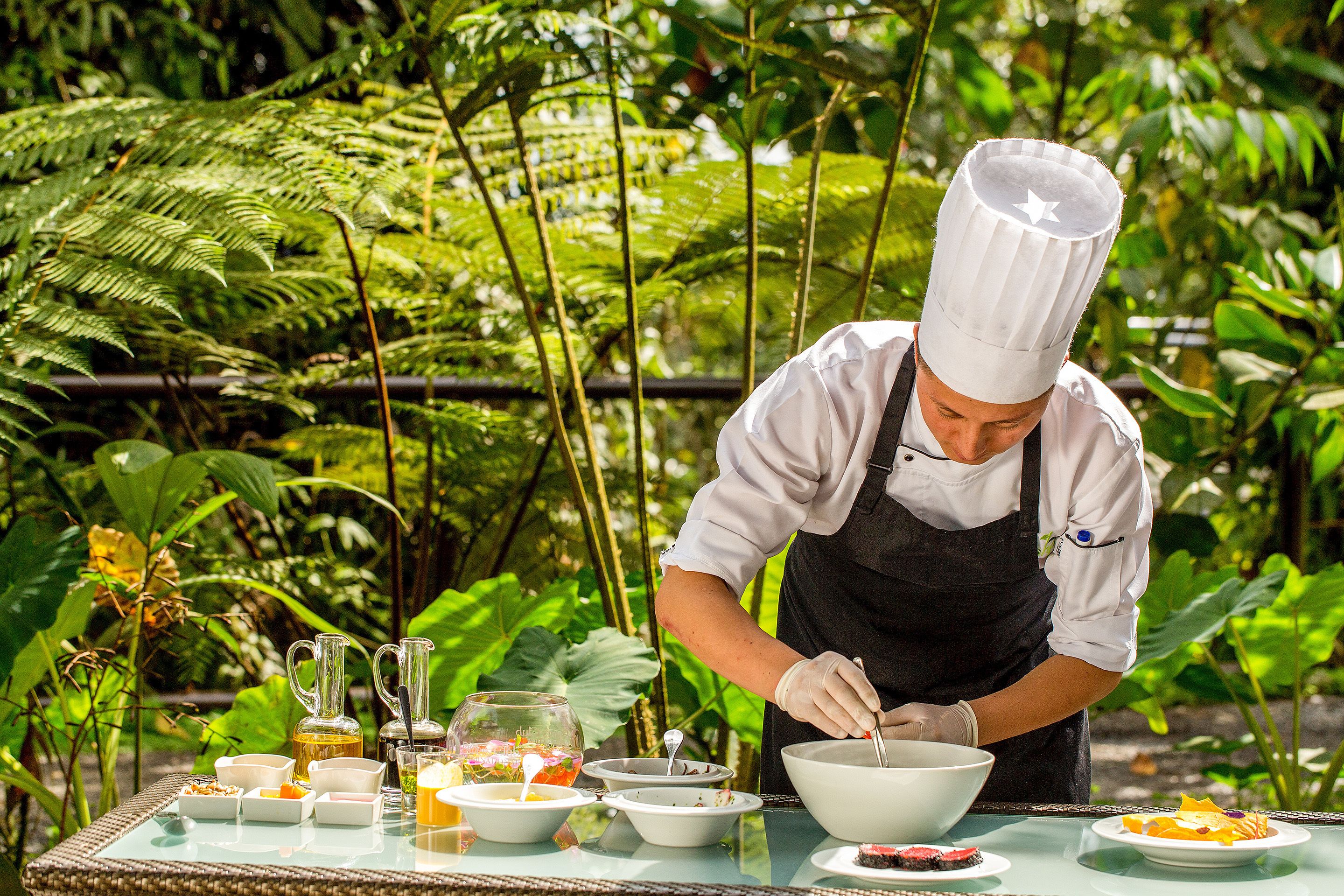 Un chef preparando comida al aire libre, con una mesa dispuesta con diferentes platos e ingredientes.
