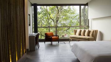 A modern hotel room with a large window, a bed, a sofa, and a desk.