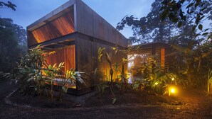 A modern building with a large open space and a sloped roof, surrounded by dense vegetation. - Mashpi Lodge (Pacto)